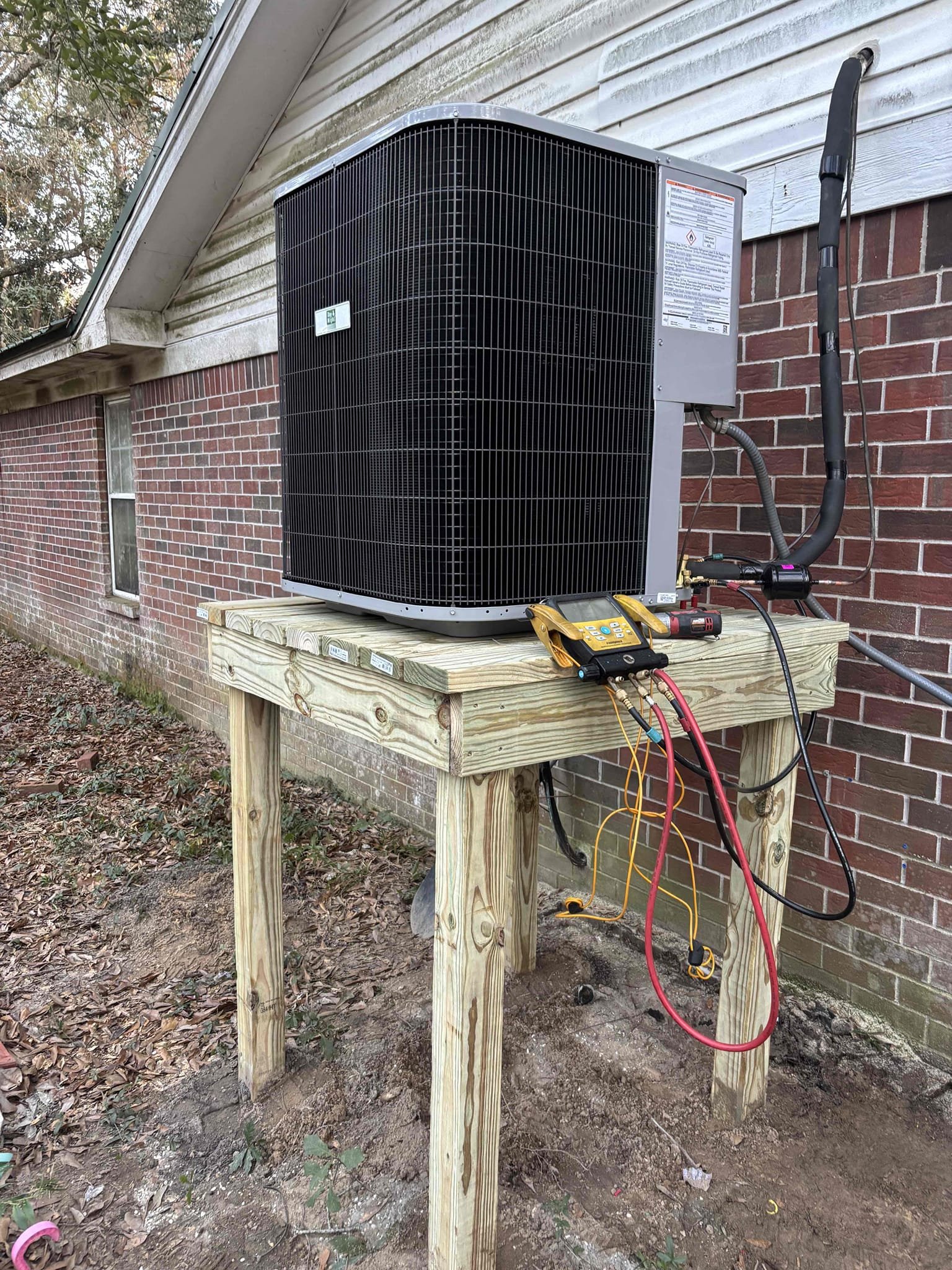 A new heat pump condenser installed on a raised wooden platform beside a brick home in Pascagoula