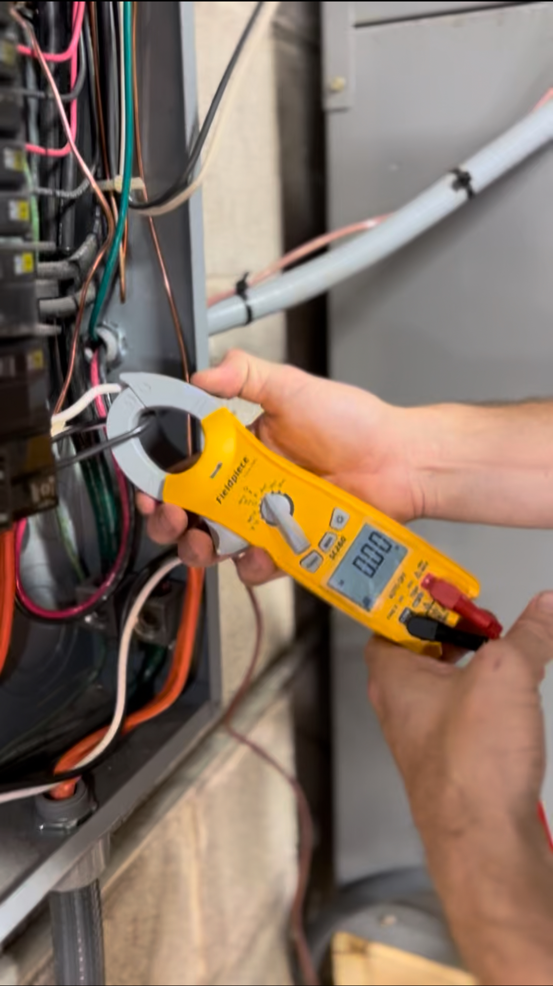 A technician testing wiring at an outdoor unit with a clamp meter during maintenance